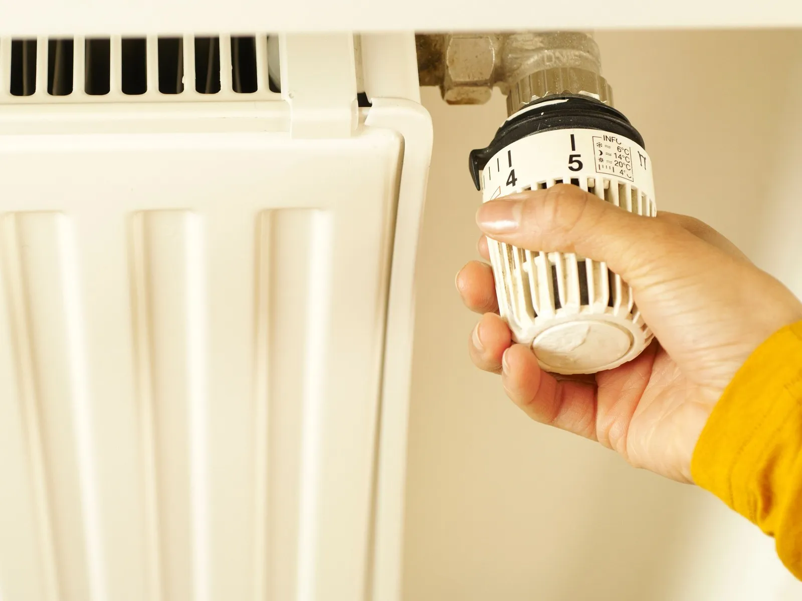 Una mano gira la valvola termostatica di un termosifone.